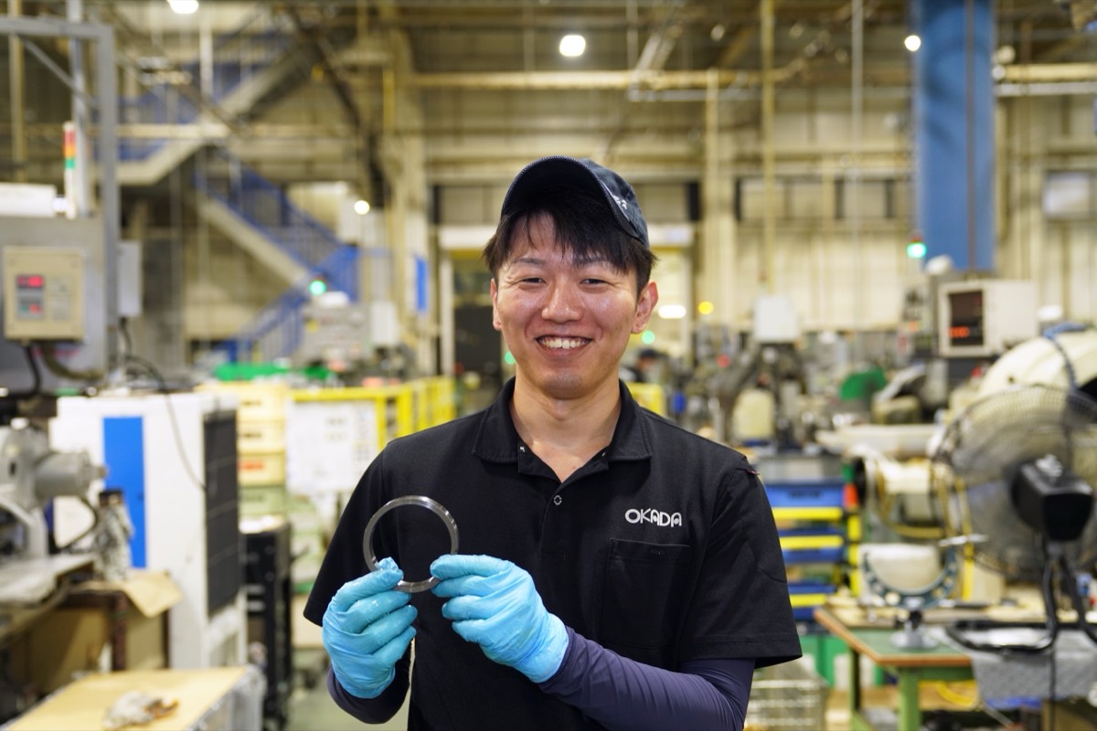 工場でまるい金属部品を仕上げるOさん